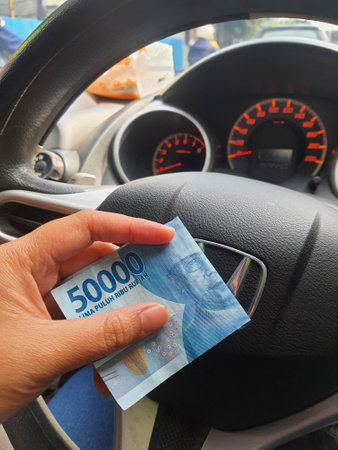 A hand is holding a fifty thousand rupiah bill which bends while driving. This money will be given to pay for cash parking.の写真素材