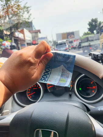A hand is holding a fifty thousand rupiah bill which bends while driving. This money will be given...