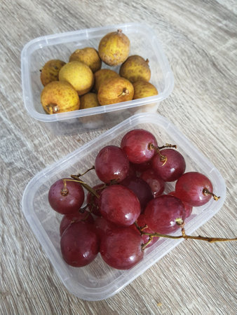Complementary food supplies for children, in the form of fruit. Two small plastic boxes containing grapes in one box and longans in the other. Contains lots of vitamins and antioxidants.の写真素材