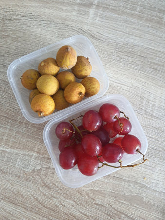 Complementary food supplies for children, in the form of fruit. Two small plastic boxes containing grapes in one box and longans in the other. Contains lots of vitamins and antioxidants.の写真素材