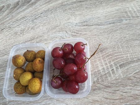 Complementary food supplies for children, in the form of fruit. Two small plastic boxes containing grapes in one box and longans in the other. Contains lots of vitamins and antioxidants.の写真素材