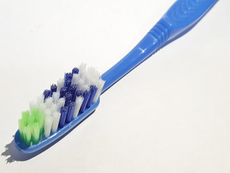 Isolated white photo of a plastic toothbrush that has been used several times. This toothbrush has a blue handle with a brush consisting of green, white and blue.の写真素材