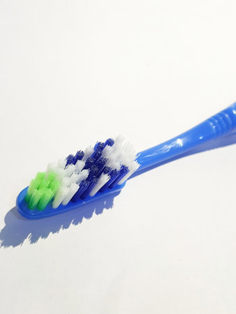 Isolated white photo of a plastic toothbrush that has been used several times. This toothbrush has a blue handle with a brush consisting of green, white and blue.の写真素材