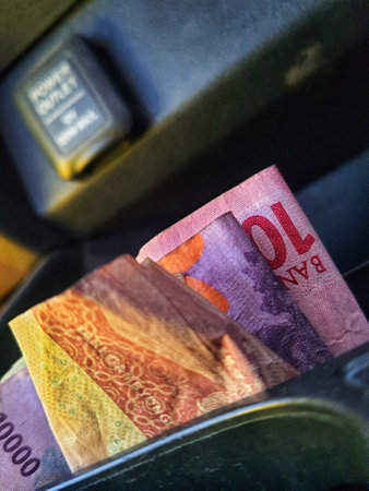 Some rupiah coins and one hundred thousand rupiah notes and some other money in a box provided on the dashboard of the car which functions as a place for coins.の写真素材