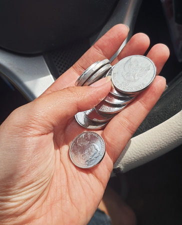 A hand is holding several rupiah coins. These coins are usually used to give to packs of people who help cross the vehicle or direct them to turn around.の写真素材