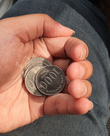 A hand is holding several rupiah coins. These coins are usually used to give to packs of people who help cross the vehicle or direct them to turn around.の写真素材
