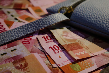 A blue wallet or blue leather pouch on top of which several hundred thousand rupiah bills are...