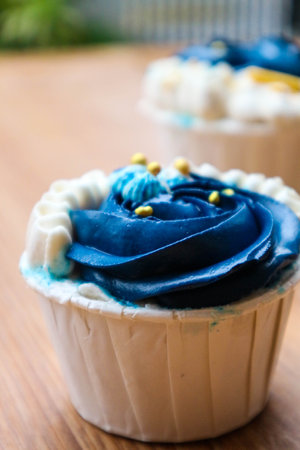 Luxurious and elegant cupcakes, with white cream and navy blue with gold sprinkles. It has a sweet and creamy taste.の写真素材
