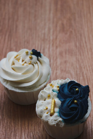 Luxurious and elegant cupcakes, with white cream and navy blue with gold sprinkles. It has a sweet and creamy taste.の写真素材