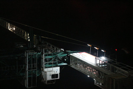 Tower crane working at night. the lighting is not too much, it only illuminates some parts of the tower crane. Tower cranes are usually used to build tall buildings.のeditorial素材