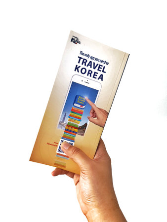 Jakarta, Indonesia in May 2022. A hand is holding a welcome guide book for travelers on vacation on Korea. The back page contains an advertisement for the KOREA TRAVEL BOOKS application.のeditorial素材