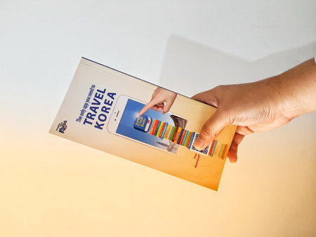 Jakarta, Indonesia in May 2022. A hand is holding a welcome guide book for travelers on vacation on Korea. The back page contains an advertisement for the KOREA TRAVEL BOOKS application.のeditorial素材