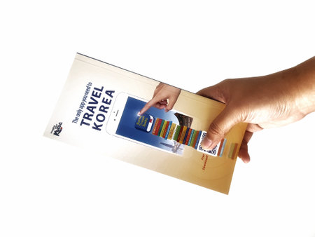Jakarta, Indonesia in May 2022. A hand is holding a welcome guide book for travelers on vacation on Korea. The back page contains an advertisement for the KOREA TRAVEL BOOKS application.のeditorial素材