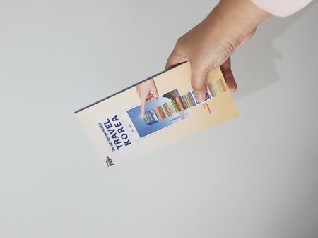 Jakarta, Indonesia in May 2022. A hand is holding a welcome guide book for travelers on vacation on Korea. The back page contains an advertisement for the KOREA TRAVEL BOOKS application.のeditorial素材