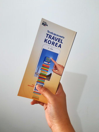 Jakarta, Indonesia in May 2022. A hand is holding a welcome guide book for travelers on vacation on Korea. The back page contains an advertisement for the KOREA TRAVEL BOOKS application.のeditorial素材