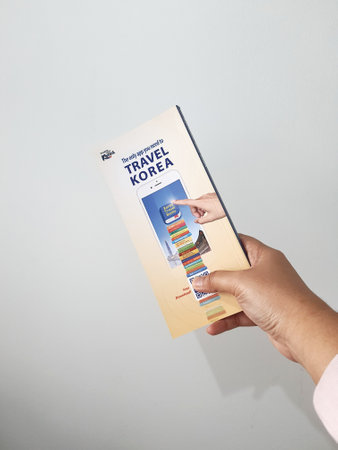 Jakarta, Indonesia in May 2022. A hand is holding a welcome guide book for travelers on vacation on Korea. The back page contains an advertisement for the KOREA TRAVEL BOOKS application.のeditorial素材