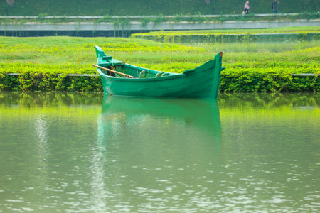 A green boat without passengers was parked on the edge of the lake. This green boat is used for maintenance of the park in the middle of the lake. A garden shaped like a map of Indonesia in Taman Mini Indonesia Indah.の写真素材