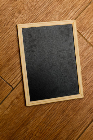 A small black chalkboard with a wooden frame rests on a brown and wooden textured floor. Perfect for your templates.の写真素材