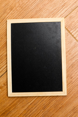 A small black chalkboard with a wooden frame rests on a brown and wooden textured floor. Perfect for your templates.の写真素材