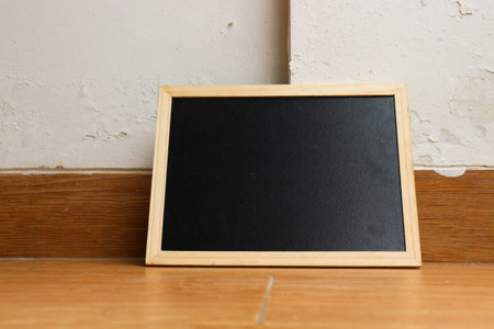 A small black chalkboard with a wooden frame rests on a brown and wooden textured floor. Perfect for your templates.の写真素材