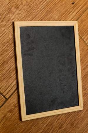 A small black chalkboard with a wooden frame rests on a brown and wooden textured floor. Perfect for your templates.の写真素材