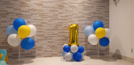 Simple first birthday boy decoration with number one balloon in gold color and balloons in yellow, dark blue, light blue, white and gray.の写真素材