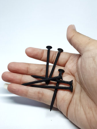 Isolated white photo of a hand carrying six black bolts with sharp ends that will be used to mount a shelf on the wall.の写真素材