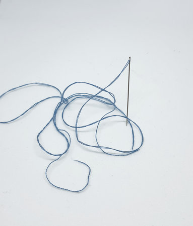 A sewing needle with a light blue thread attached to it. Needles stand upright, ready for sewing.の写真素材
