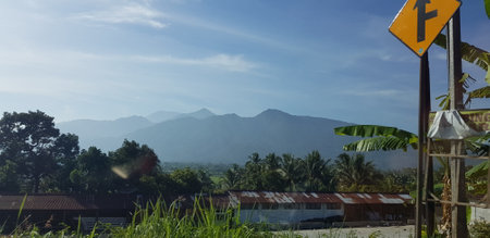 A view of green rice fields and gardens with blue sky and white clouds. You can see the silhouette of a mountain behind him. This view is the view when on the way to Yogyakarta.の写真素材
