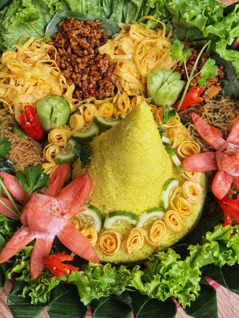 The Nasi Tumpeng contains beautifully decorated yellow rice with various side dishes, namely orek tempeh, stir-fried chicken, scrambled eggs, shredded meat and various kinds of vegetables.の写真素材