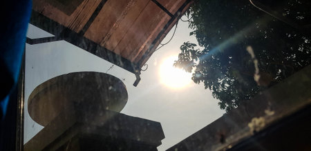 Reflecting sunlight passing through the bedroom window, partly covered by the leaves of shady trees, you can see the roof and a large pot.の写真素材