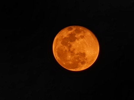 A fiery orange moon dominates the night sky, its surface textured with craters, casting an intense, almost mystical glow.の写真素材