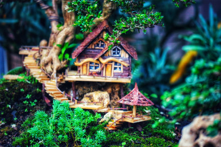 A charming miniature treehouse nestled in a lush bonsai garden.  Wooden walkways wind through vibrant green moss, creating a tranquil, fairytale-like atmosphere.の写真素材