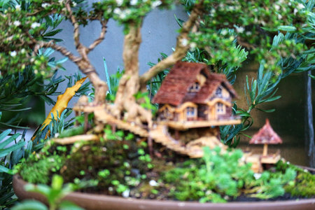 A charming miniature house sits nestled within a vibrant bonsai tree, creating a serene and enchanting miniature garden.  Tiny details and lush greenery evoke a peaceful mood.の写真素材