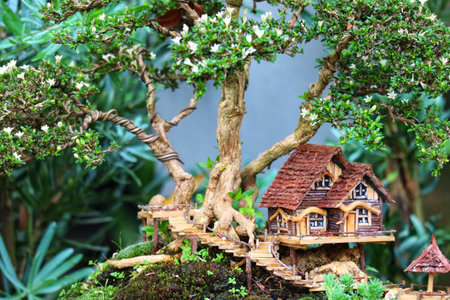 A charming miniature cottage sits nestled amongst the branches of a vibrant bonsai tree, creating a serene and enchanting miniature world.  Wooden stairs lead up to the cozy house, surrounded by lush greenery.の写真素材