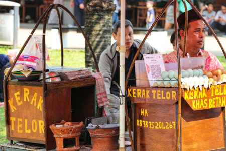 Two rustic food carts sell Kerak Telor on a sunny day.  A vendor smiles, eggs ready, creating a vibrant and bustling street scene.の写真素材