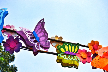 A cheerful string of vibrant paper butterflies and flowers dances against a clear blue sky.  The playful design creates a joyful, sunny mood.の写真素材