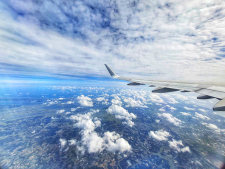 A breathtaking aerial view from an airplane window showcasing a vast expanse of fluffy white clouds spread across a deep blue sky. The airplane wing is partially visible in the foreground, adding a sense of scale and perspective to this stunning landscape seen from above. The image captures a peaceful and serene atmosphere.の写真素材