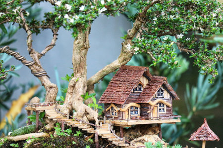 A charming miniature house nestled in a lush bonsai tree, creating a whimsical and peaceful atmosphere.  Wooden details and winding stairs add to the enchanting scene.の写真素材