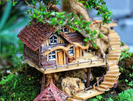 A whimsical miniature log cabin nestled in a lush bonsai tree, complete with a winding wooden staircase and mossy base, evokes a peaceful, enchanting scene.の写真素材