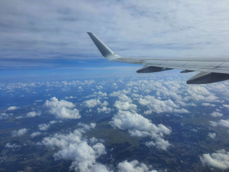 A stunning aerial view from an airplane window showcases a vast expanse of fluffy white clouds spread across a dark blue landscape below.  The airplane's white wing is prominently featured in the foreground, offering a sense of scale and height. The overall mood is serene and peaceful.の写真素材