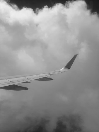 A black and white photo captures an airplane wing in flight above a dense cloud layer The image emphasizes the wing's design against the textured sky providing a sense of aerial perspective and atmospheric depthの写真素材