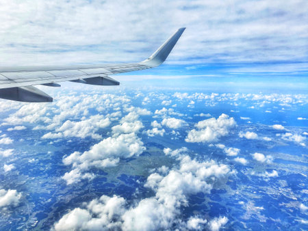 A stunning aerial view from an airplane window showcasing a vast expanse of fluffy white clouds below a clear blue sky.  The airplane wing is partially visible in the foreground, adding a sense of height and travel.  The overall mood is serene and peaceful.の写真素材