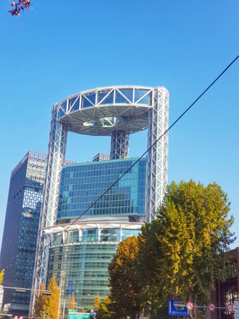 Seoul, South Korea on 12 Nov 2024. A striking modern tower dominates the scene, its glass facade reflecting a clear blue sky. A circular skydeck adds a unique architectural detail, while autumn trees provide a warm contrast. The overall mood is serene and sophisticated.の写真素材