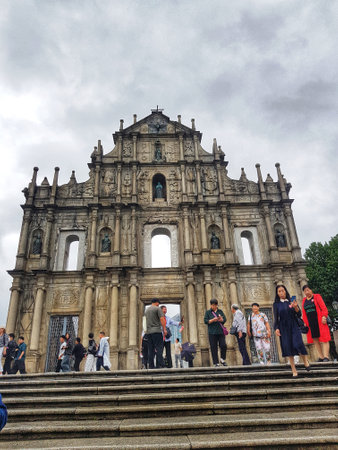 Santo Antonio, Macau on 14 Nov 2024. Awe-inspiring! The weathered stone of St. Paul's facade stands tall under a cloudy sky. Tourists ascend the steps, admiring its Baroque artistry and somber beauty.の写真素材
