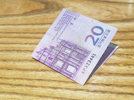 Macau, China on 14 Nov 2024. A partially folded twenty pataca note rests on a wood surface. The intricate design features a church and is in subtle purples. A serene and slightly formal mood.の写真素材