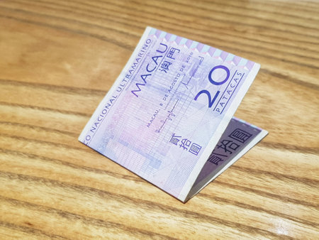 Macau, China on 14 Nov 2024. A crisp twenty patacas Macau banknote rests on a warm wood surface, its intricate design subtly highlighted by the soft light. The folded bill evokes a sense of elegance and understated value.の写真素材