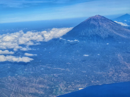 A stunning aerial perspective shows a grand volcano, a sprawling green landscape, and the endless blue ocean, ideal for travel and nature publications.の写真素材