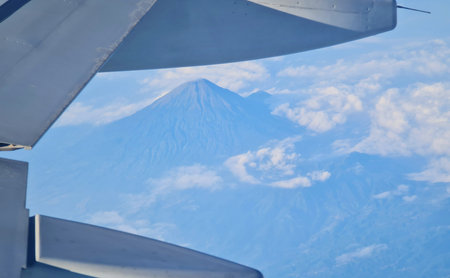 View from airplane window reveals majestic mountain surrounded by clouds and blue sky Great for...