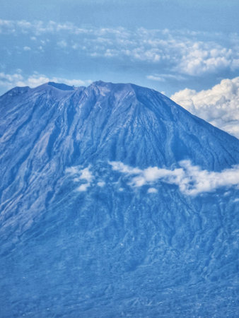 This aerial shot showcases a breathtaking mountain peak partially veiled in clouds against a clear blue sky Perfect for travel and nature-themed projects.の写真素材